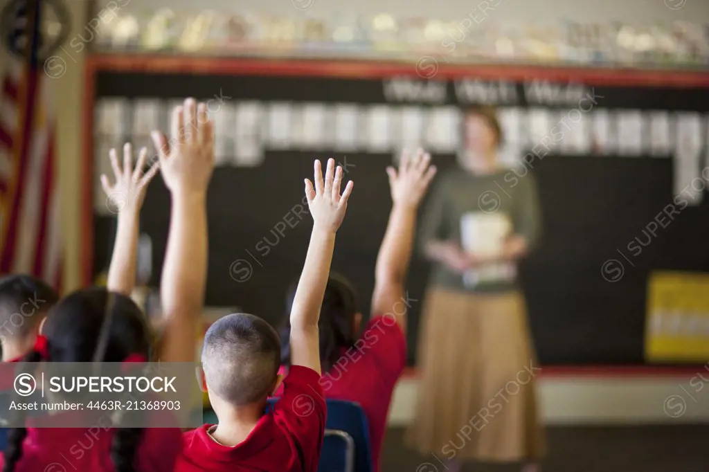 Students with their hands raised in a classroom.