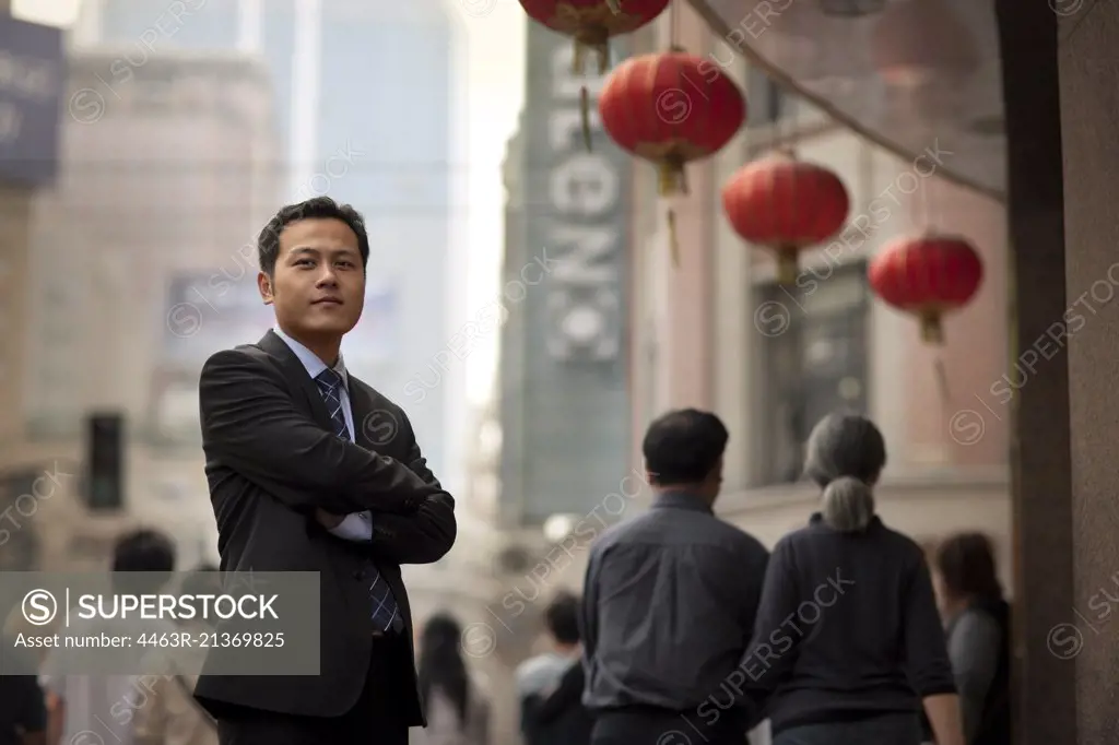 Portrait of a mid adult businessman standing in a busy street with his arms folded.