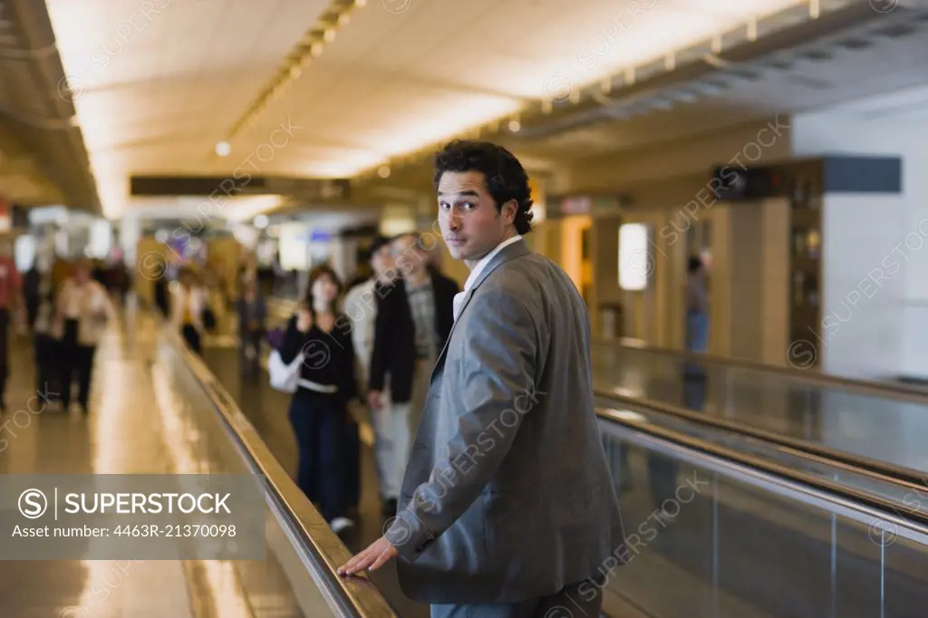 Portrait of a young businessman looking over his shoulder while riding a travel platform in an airport.