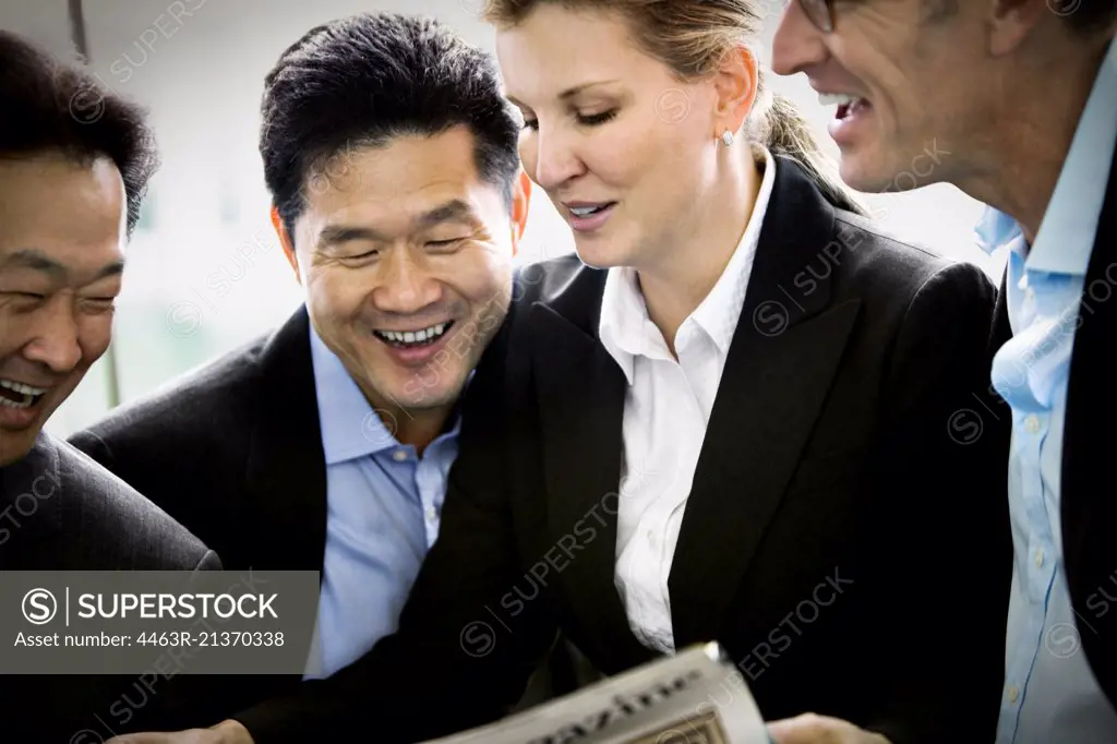 Mid-adult business colleagues laughing at a newspaper.