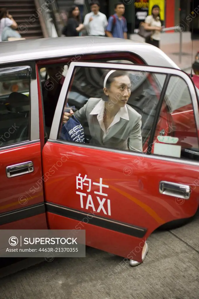 Young adult business woman exiting a taxi in a city.