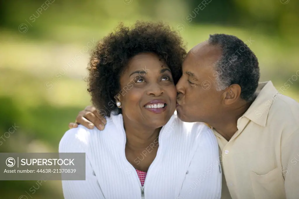 Happy mature man gives his smiling wife a kiss on the cheek.