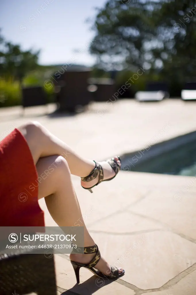 Legs of a woman sitting poolside at her house.