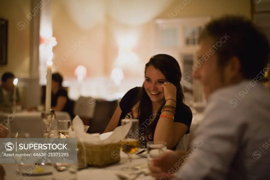 Teenage girl sitting at a dining table in a restaurant with her family.