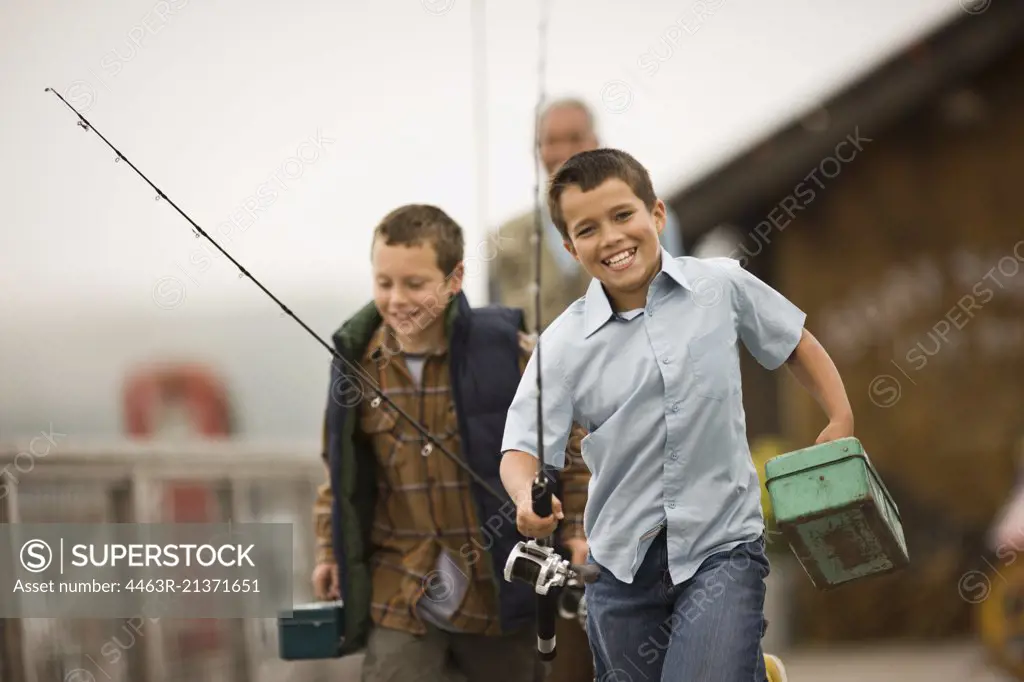 Exited boy running down a wharf carrying fishing gear with his father and brother