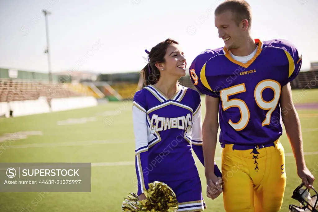 Football player and cheerleader holding hands on football field