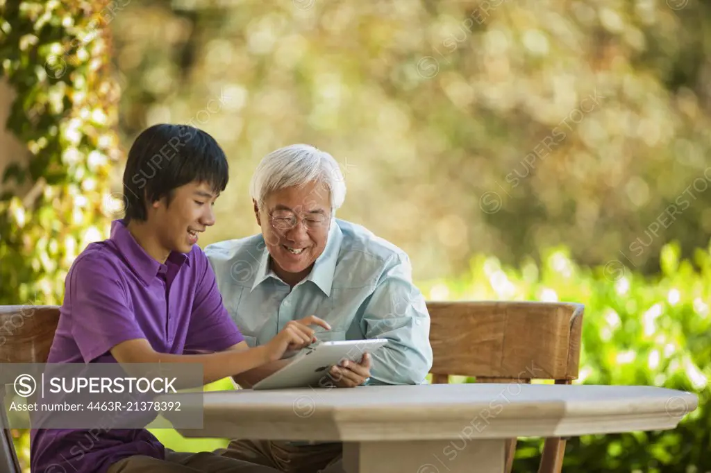 Smiling teenage boy showing his grandfather how to use a digital tablet.