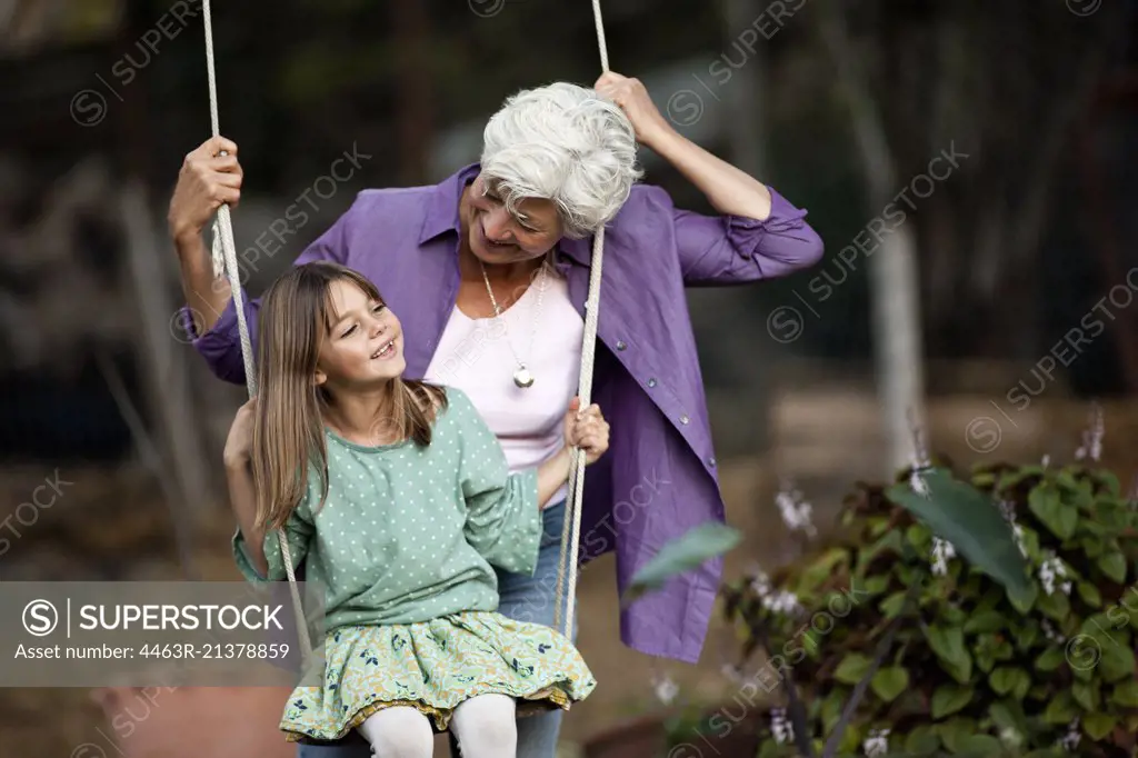 Senior woman pushes her granddaughter on a swing. 