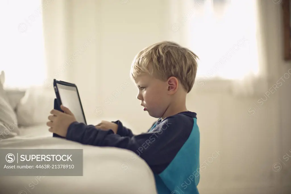Young boy looking serious as he plays with a portable information device. 