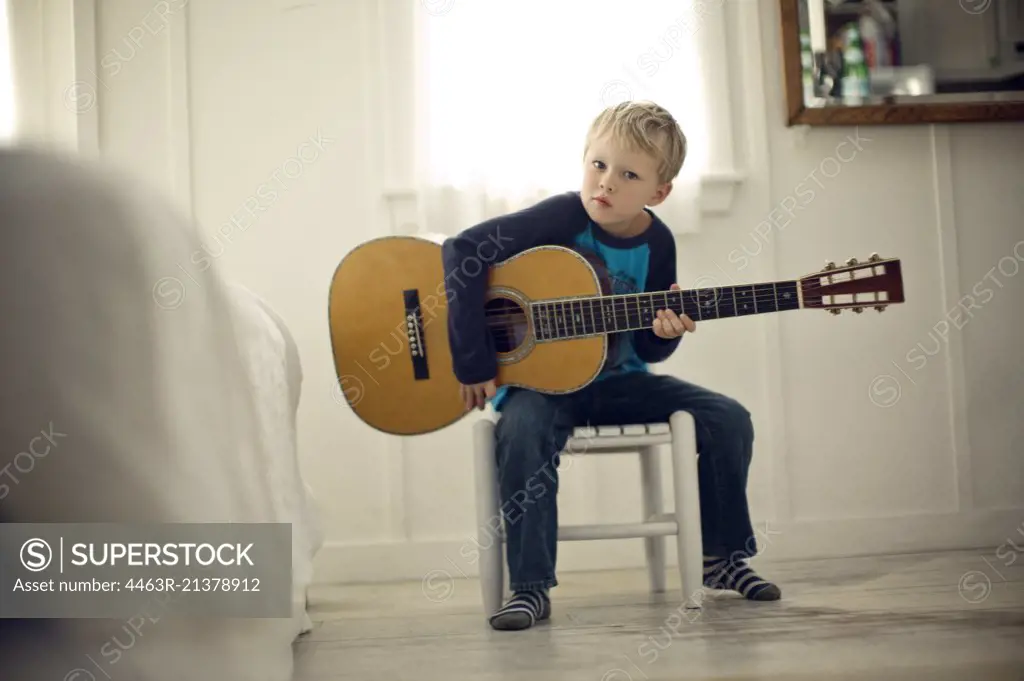 Young boy sits on a chair holding an acoustic guitar. 