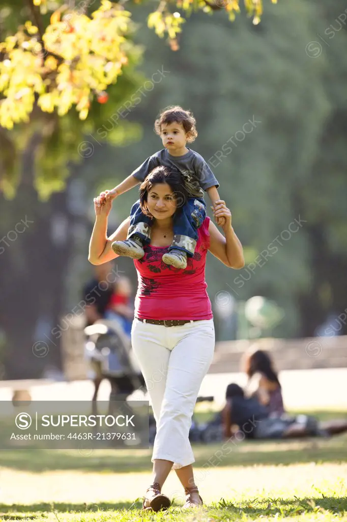 Middle aged mother carries her son on her shoulders.