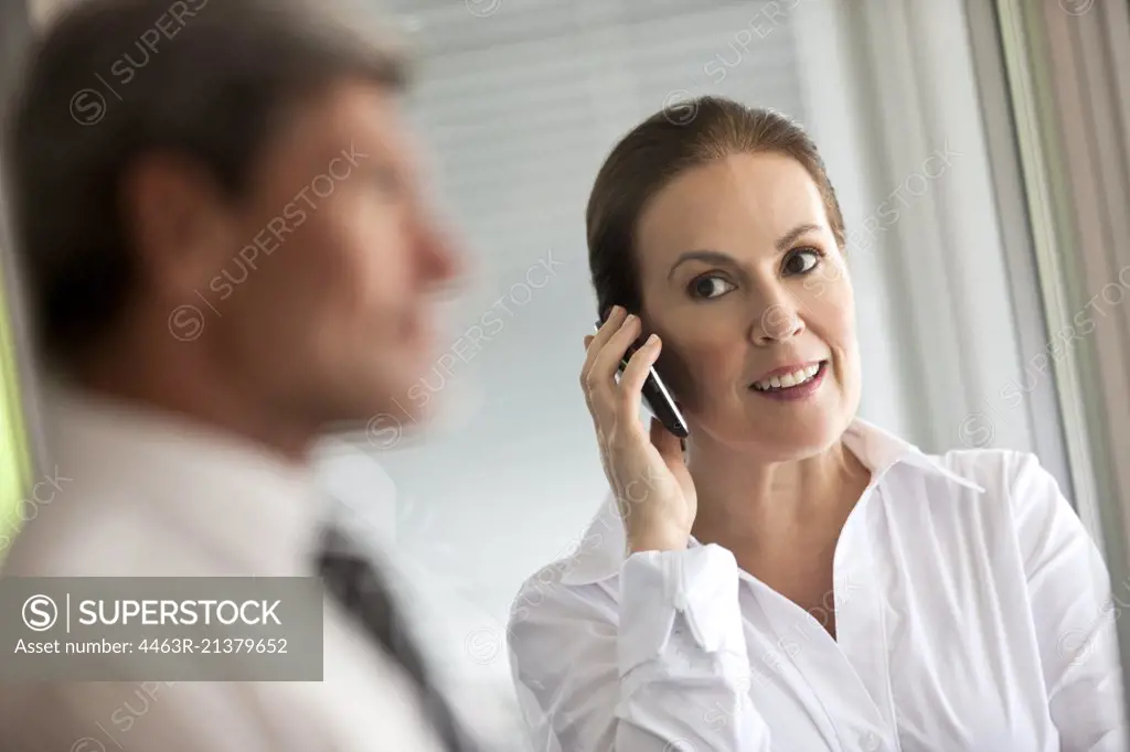 Businesswoman takes a call on a cell phone and looks at a male colleague waiting for her.