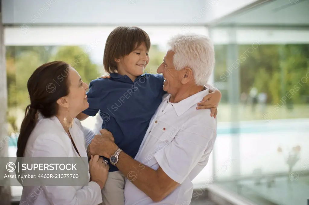 Senior couple smile and hug their grandson.