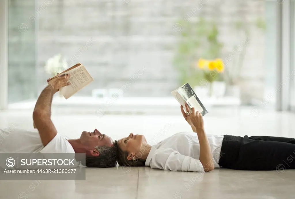 Couple lying on living room floor, reading a book. 