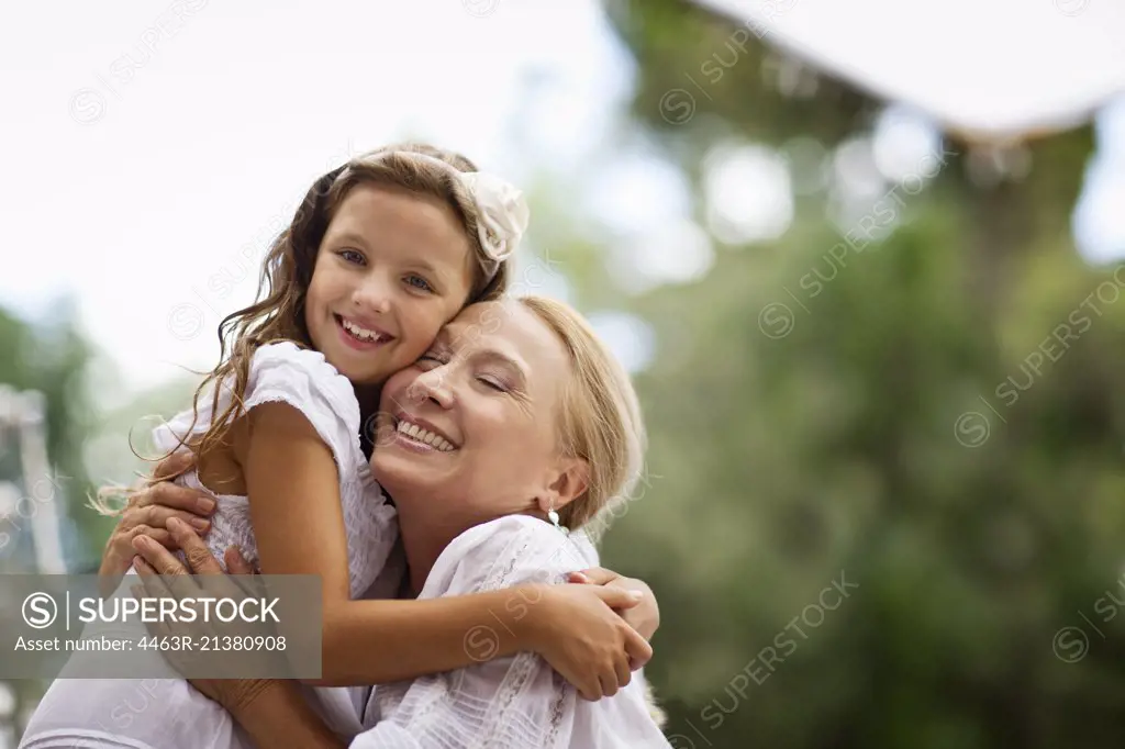 Grandmother embraces her granddaughter outdoors.