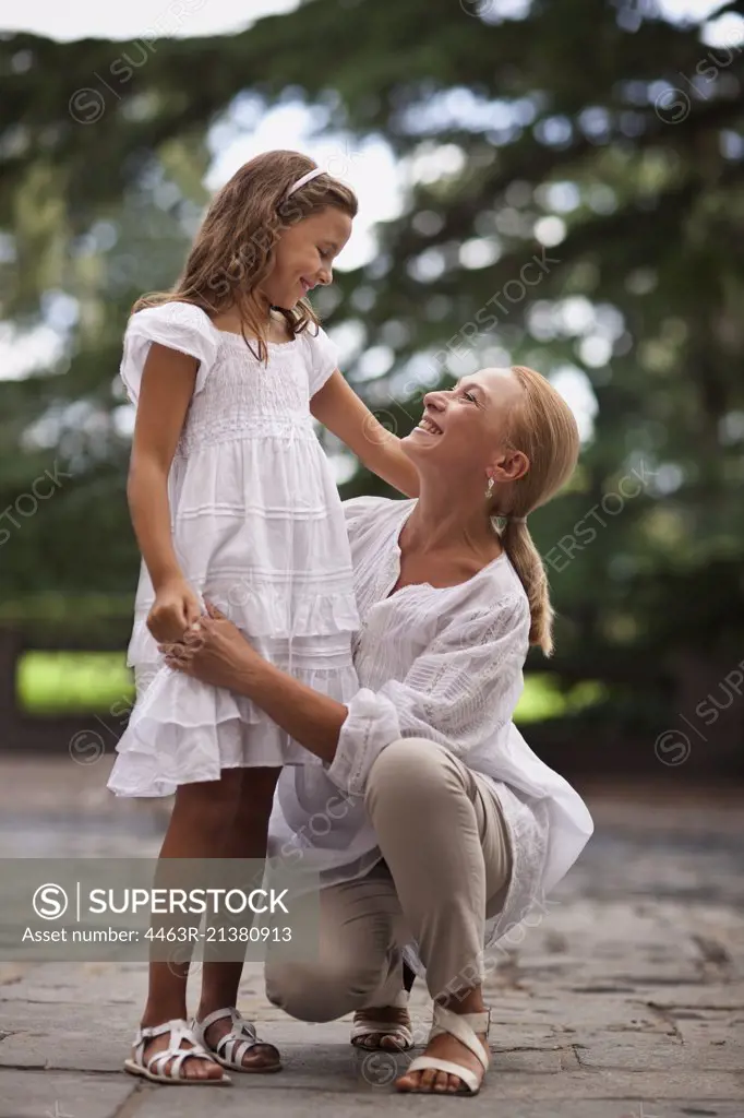 Grandmother crouches beside her young granddaughter and holds her hand outdoors.