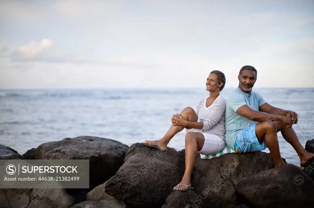 Portrait of mature couple sitting back to back waterside.