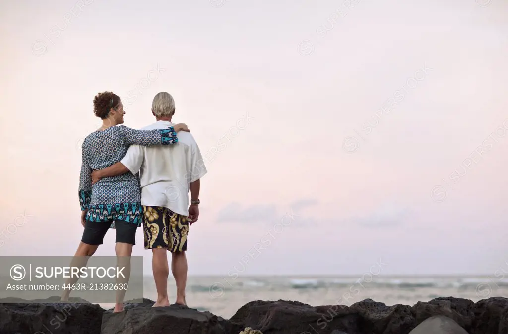 Couple standing together on rocks with arms around each other. 