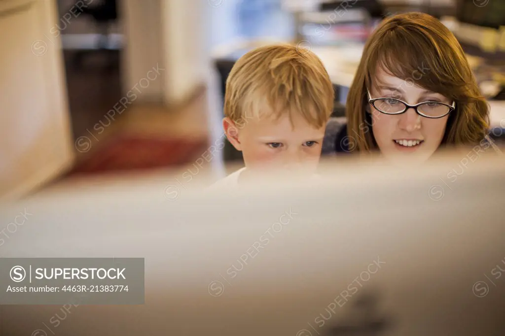 Young boy and his mother looking at a computer monitor.