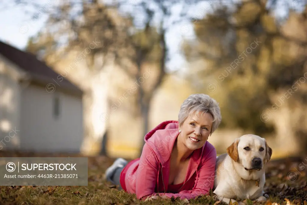Portrait of a smiling senior woman lying on her front in a field with her dog.