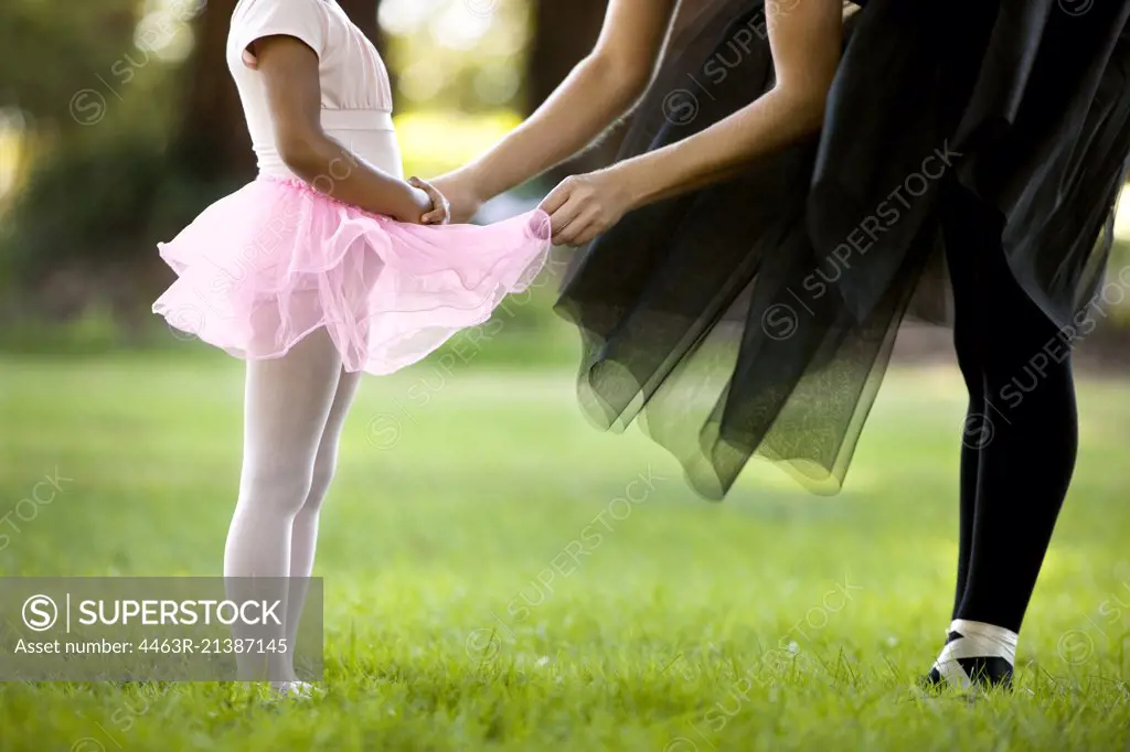 Mid adult woman and her young daughter ballet dancing in a park.
