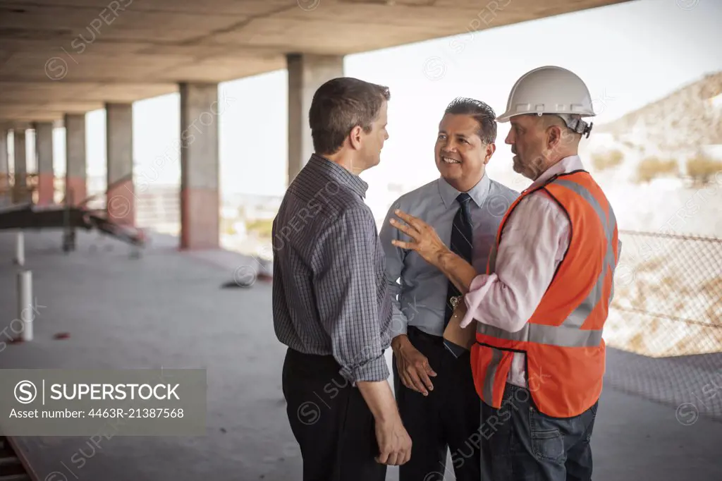 A construction manager and two executives talking on construction site.