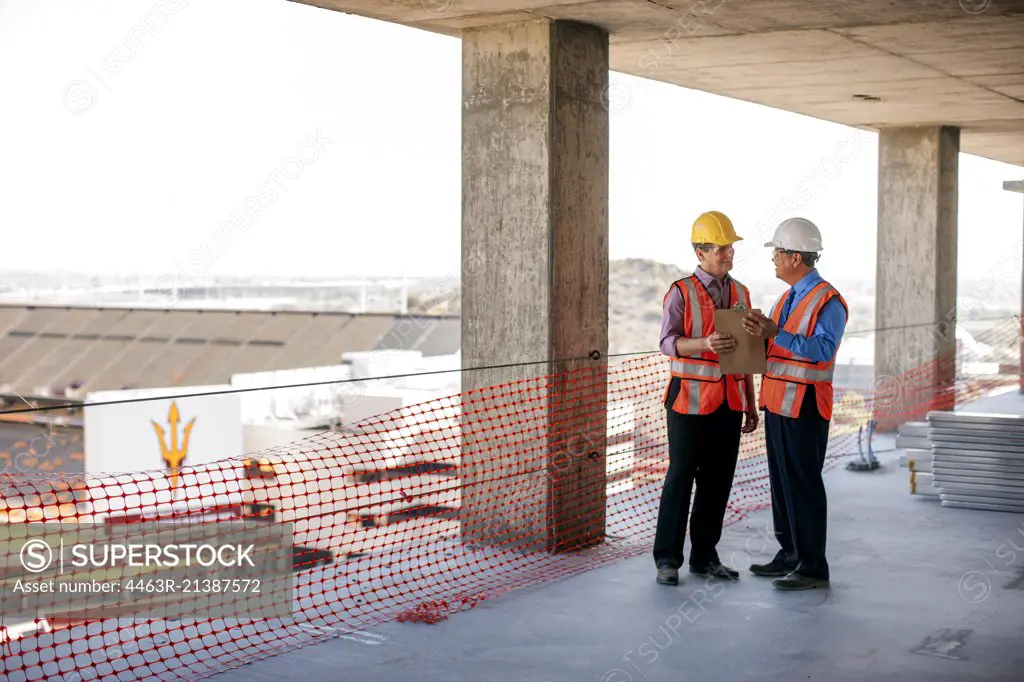 Two executives in safety gear talk on construction site.