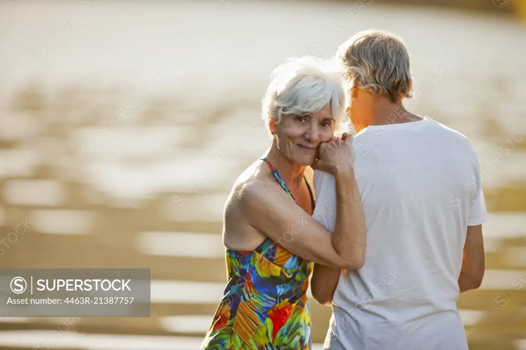 Portrait of a smiling senior woman leaning on the shoulder of her husband next to a lake.