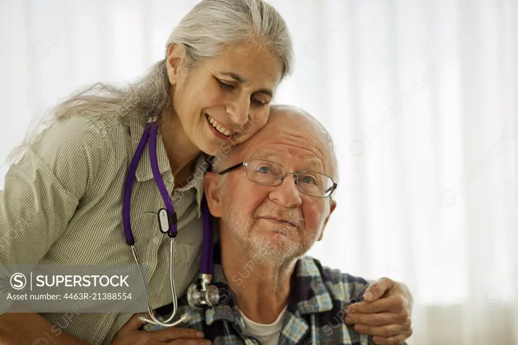 Doctor standing with her arms around an elderly patient.