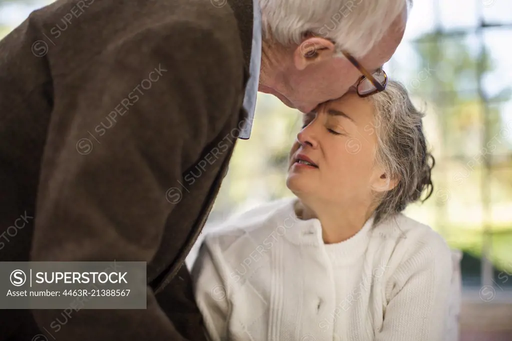 Elderly man kisses his wife on the forehead.