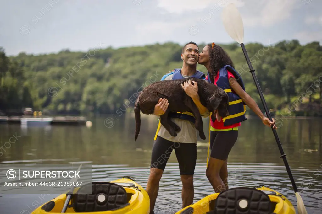 Young kayaker kissing her boyfriend's cheek while he holds a dog.
