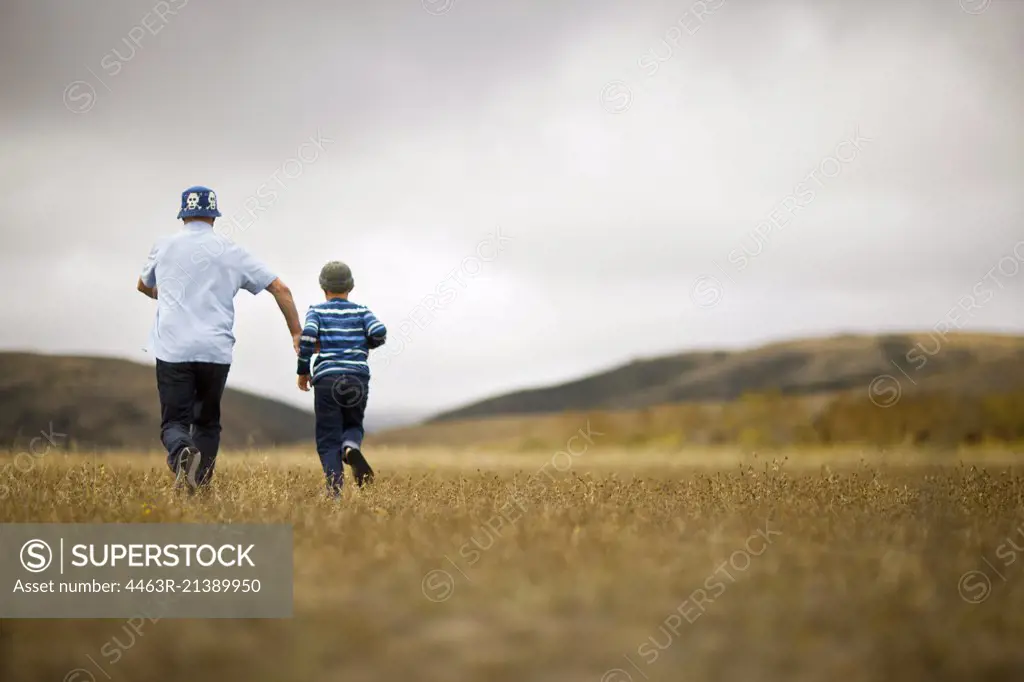Young boy and father running through a grassy field.