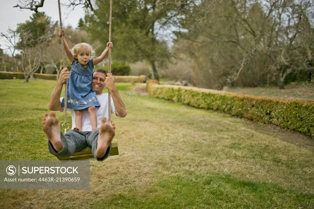 Little girl looks uncertain as she swings on a tree swing with her father.