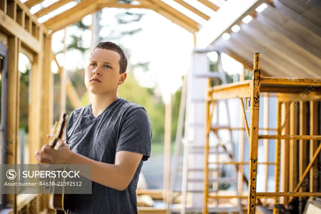 Contented teenage boy playing a mandolin at a construction site.