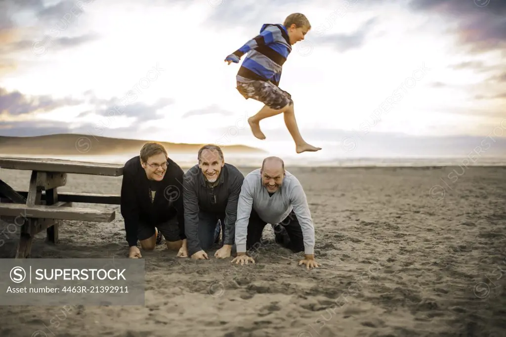 Playful young boy leaping over three kneeling men.