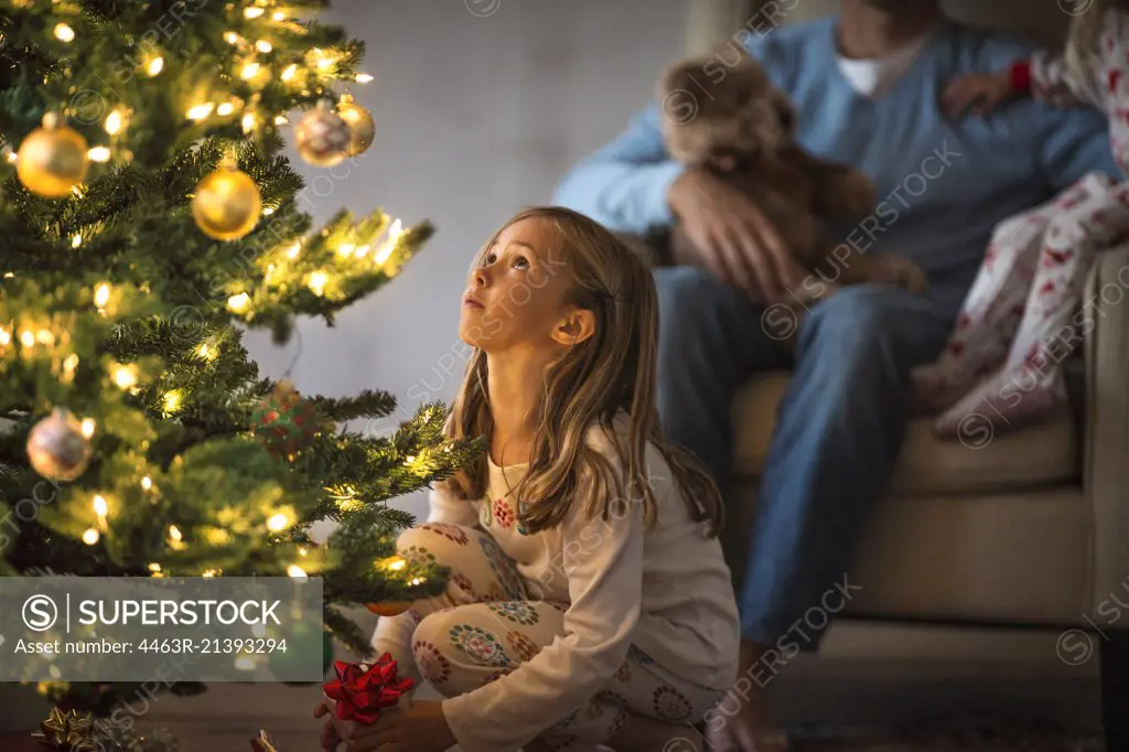 Young girl looking up at a decorated and illuminated Christmas tree.