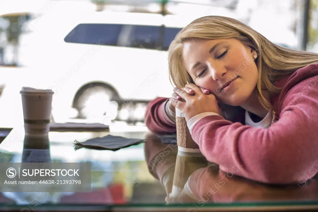 Tired young woman resting her head on her coffee cup.