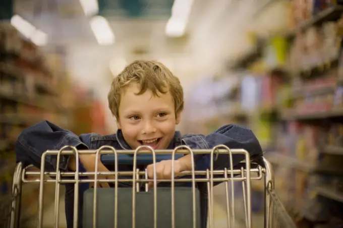 Smiling young boy pushing a trolley at a supermarket.