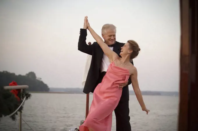 Mature adult couple dressed formally and dancing on a boat.