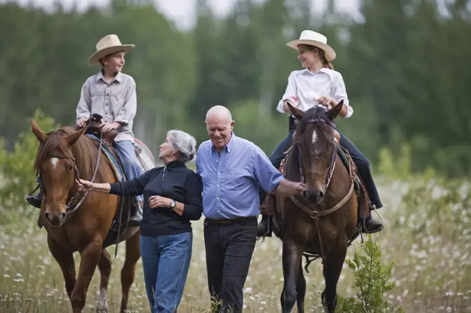 Grandparents leading horses ridden by grandchildren