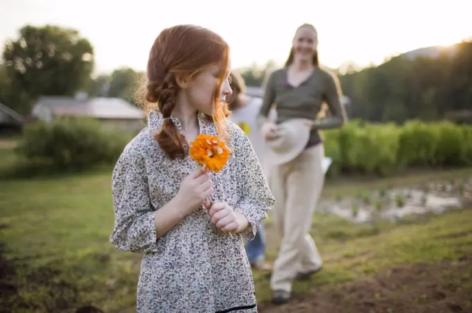 Young girl holding a flower as her mid-adult mother looks on while on a farm.