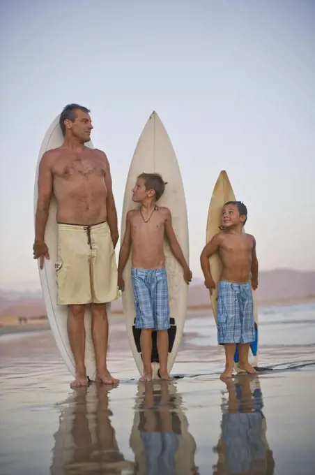 Father and his two sons posing with their surfboards at the beach