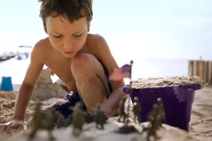 Young boy building sandcastles and playing with toys on a beach.