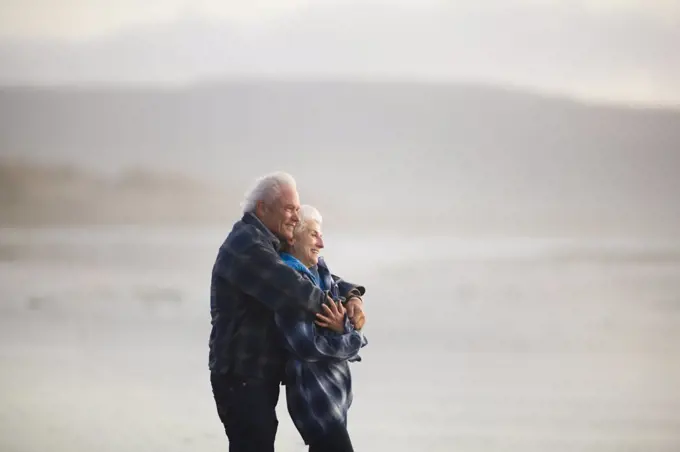 Happy mature couple standing with their arms around each other on a remote beach.