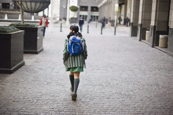 Teenage schoolgirl with a backpack walking along a cobbled street in the city.
