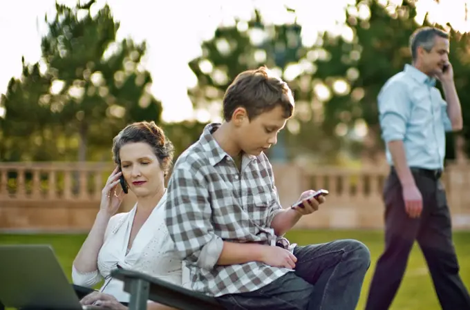 Boy text messaging on his cellphone while his parent are busy on their own cellphones.