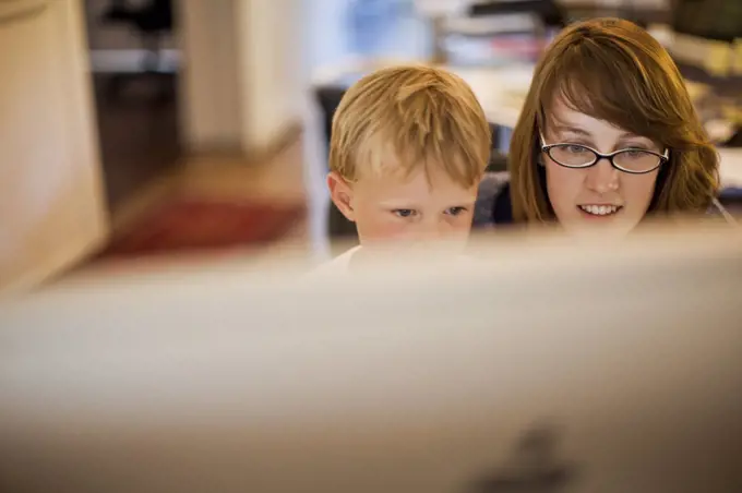 Young boy and his mother looking at a computer monitor.