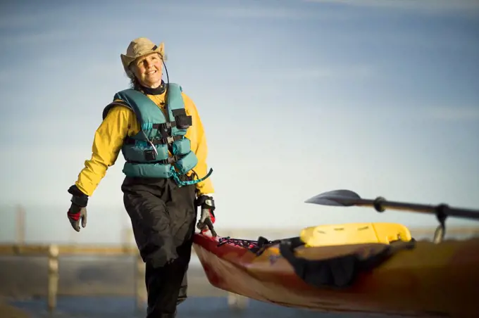 Smiling senior woman carrying the end of a kayak in the sunshine.
