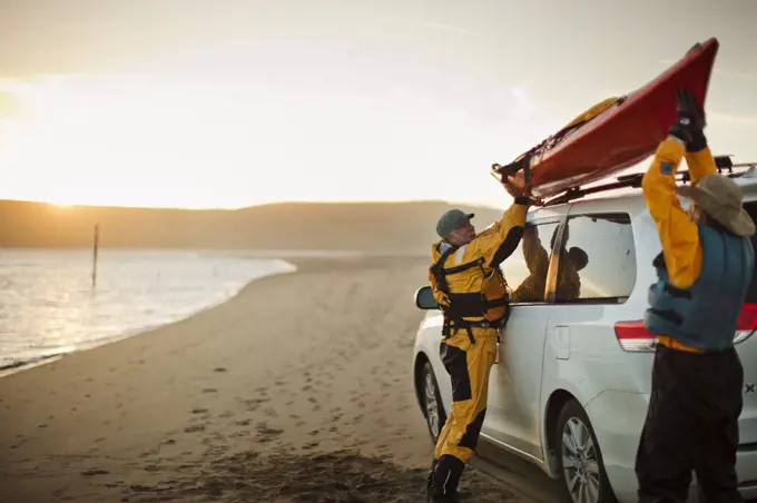 Happy senior couple lifting a sea kayak onto the roof of a SUV parked on a sandy beach.
