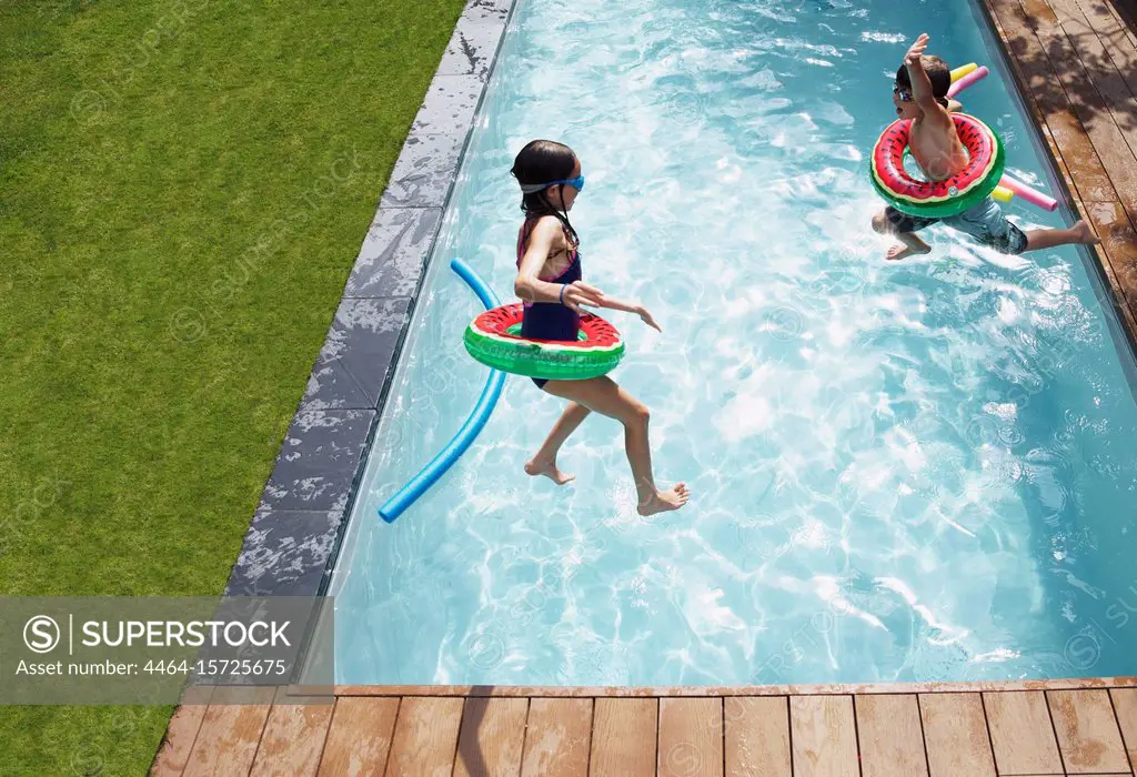 Boy and girl jumping into sunny summer pool